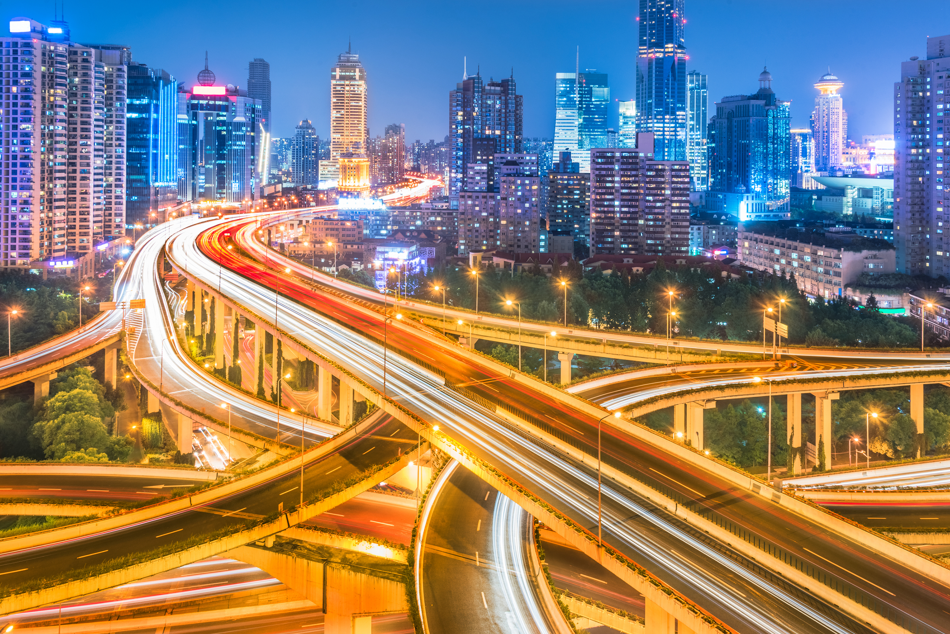 An_aerial_view_of_a_vibrant_city_at_night,_featuring_a_sprawling_network_of_highways_and_overpasses._The_long_exposure_creates_streams_of_light_from_vehicles,_giving_a_dynamic_sense_of_motion._Skyscrapers_with_brightly_lit_windows_and_neon_signs_fill_the_background,_highlighting_the_city's_bustling_energy_and_modern_architecture.