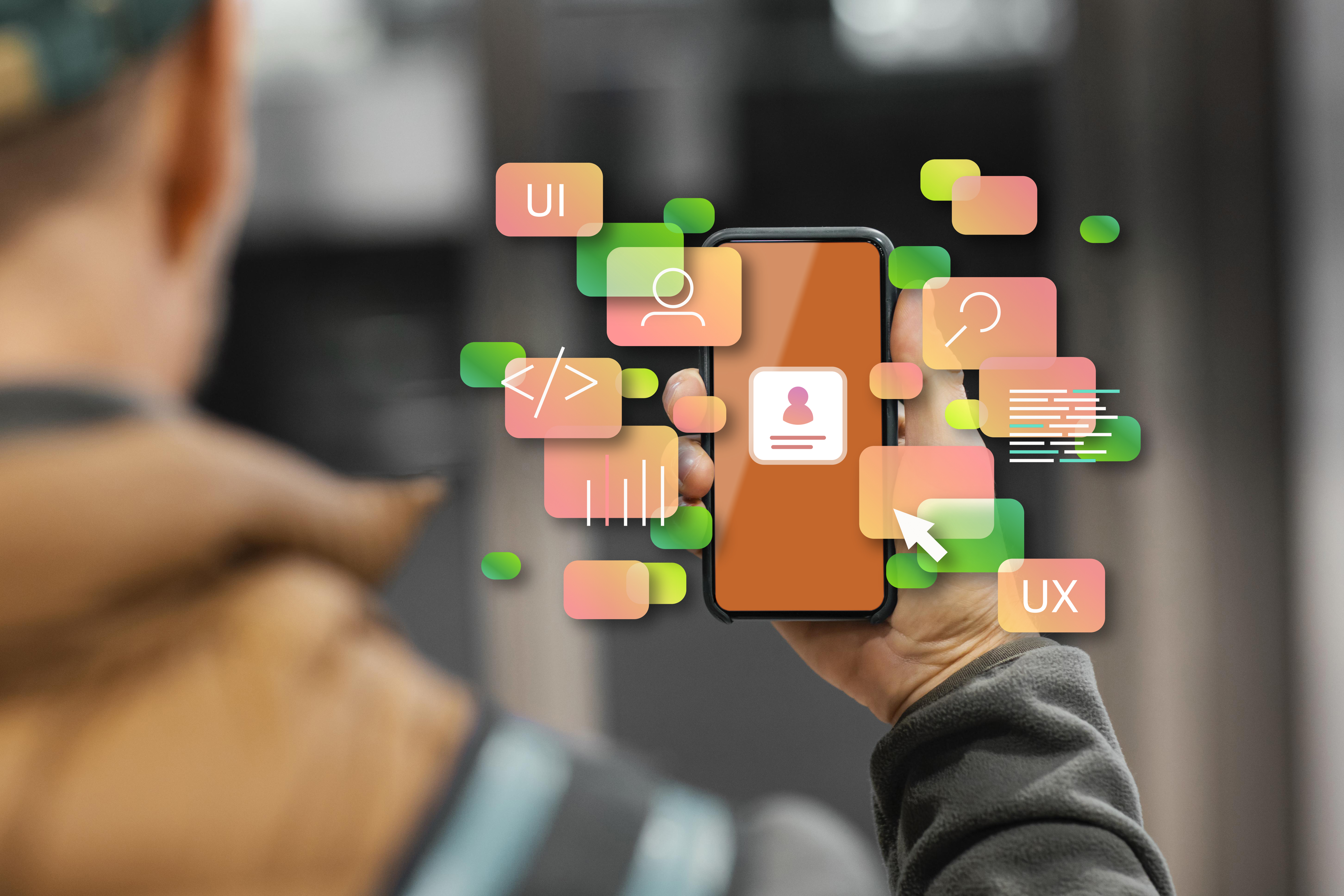 A_person_holds_up_a_smartphone_with_digital_elements_floating_around_the_screen._The_screen_displays_a_profile_icon,_while_various_colorful_icons_representing_UI,_UX,_coding,_and_graphs_surround_the_device._This_visual_represents_user_interface_and_user_experience_design,_emphasizing_mobile_app_development_and_interactive_features.